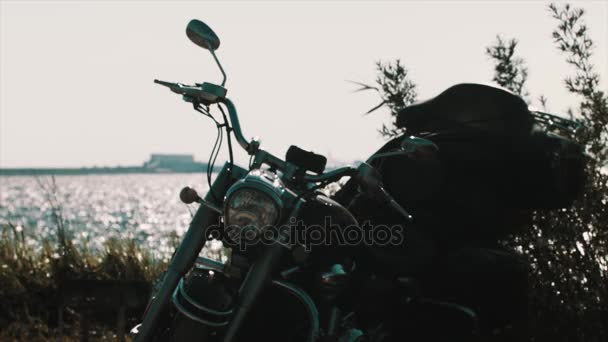 Zwarte chopper motorfiets geparkeerd in de struiken op de oever van de zee — Stockvideo