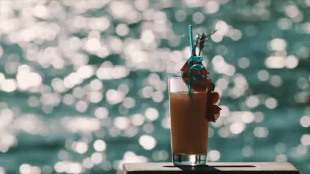 Orange cocktail with fancy decorations in front of shiny water surface — Stock Video