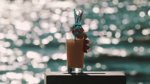 Orange cocktail with fancy decorations in front of shiny sea surface — Stock Video
