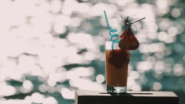 Orange cocktail with fancy decorations in front of shiny ocean surface — Stock Video