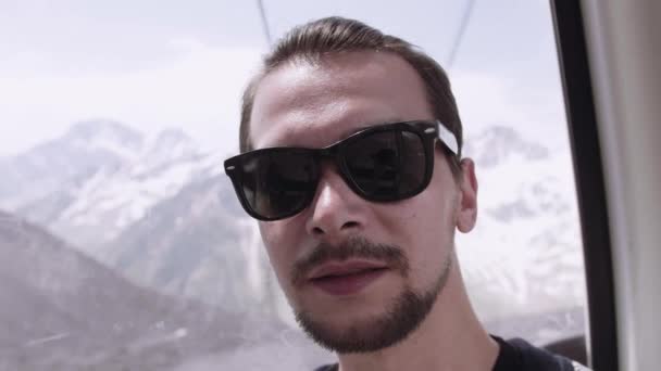 Giovane uomo barbuto in occhiali da sole cavalcando ascensore aereo a zona picche innevate — Video Stock