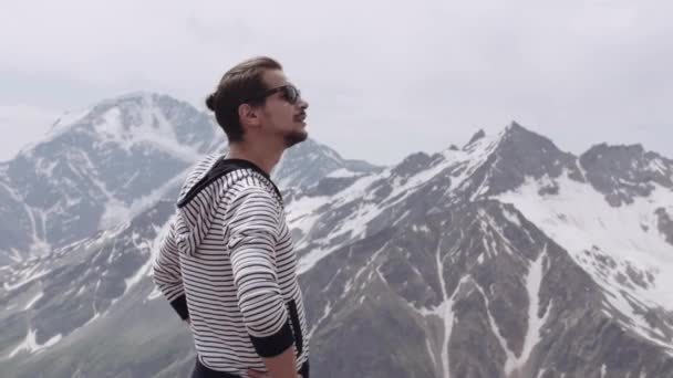 Young man in striped hoodie and sunglasses looking around at mountain see sight — Stock Video