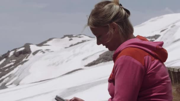 Woman in pink hoodie texting on smartphone at mountain campsite — Stock Video