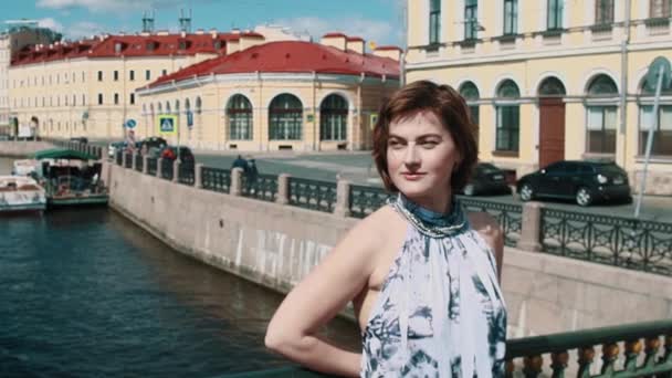 Wanita muda melihat sekeliling tersenyum di jembatan kota di atas sungai — Stok Video