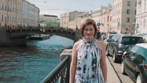 Jonge vrouw in gevlekte jurk wandelingen langs de rivier in het oude centrum van de stad — Stockvideo