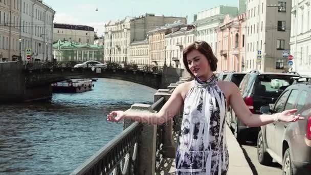 Mooie jonge vrouw in gevlekte jurk zingt op de dijk in het oude centrum van de stad — Stockvideo