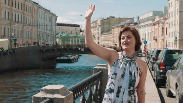 Vrolijke jonge vrouw in gevlekte jurk zingt op de dijk in het oude centrum van de stad — Stockvideo