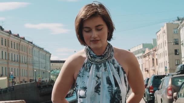 Cheerful girl in spotted dress sings at embankment in old town centre — Stock Video