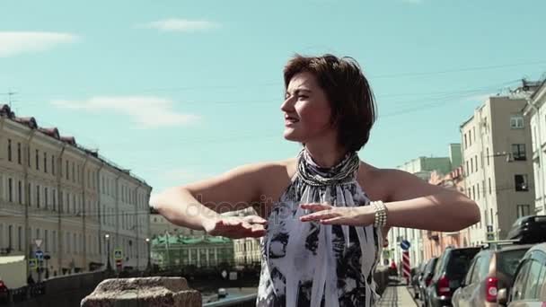 Χαρούμενο κορίτσι κύματος τα χέρια κινούνται τα δάχτυλα στην παλιά πόλη, στον ποταμό — Αρχείο Βίντεο
