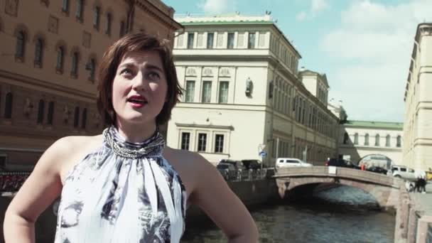 Wanita cantik bergaun terang bernyanyi di sepanjang sungai di pusat kota tua — Stok Video