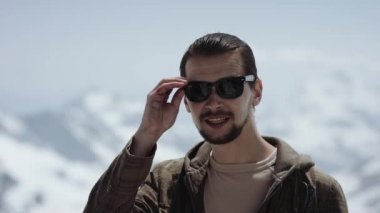 Genç adam dağın zirvesinde doğal görünümü savunarak ile güneş gözlüğü sakallı