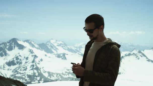 Joven barbudo recibe llamada telefónica en las montañas nevadas con vista panorámica — Vídeos de Stock