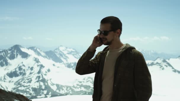 Joven barbudo hablando por teléfono móvil en las montañas nevadas con vista panorámica — Vídeos de Stock