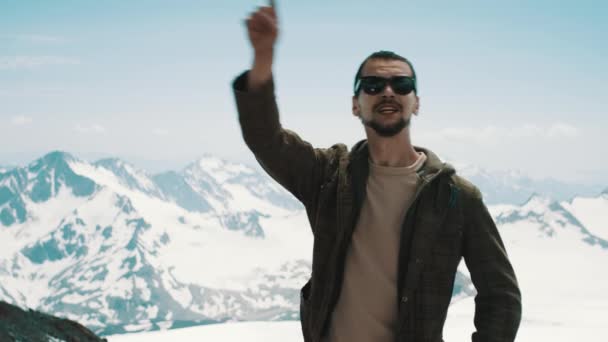 Молодой бородатый мужчина указывает на вершины снежных гор с живописным видом — стоковое видео