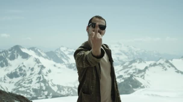 Giovane uomo barbuto mostra dito medio a montagne innevate con vista panoramica — Video Stock