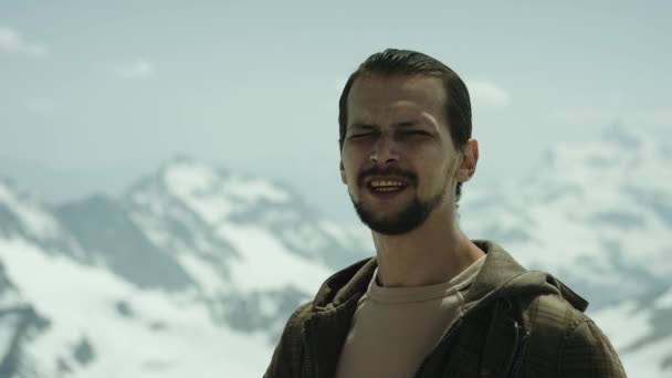 Young bearded man at mountain summit with scenic view squint eyes and talking — Stock Video