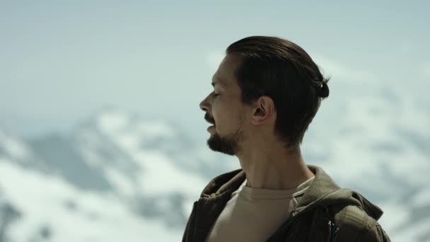 Hombre barbudo joven en el pico de la montaña con vista panorámica respiración profunda y mirar hacia otro lado — Vídeo de stock