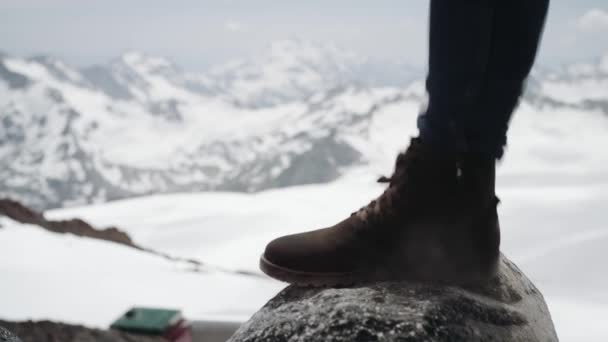 Πεζοπόρος πόδια σε Δερμάτινη μπότα stomps στην πέτρα στο χιονισμένο βουνό, γραφική θέα — Αρχείο Βίντεο