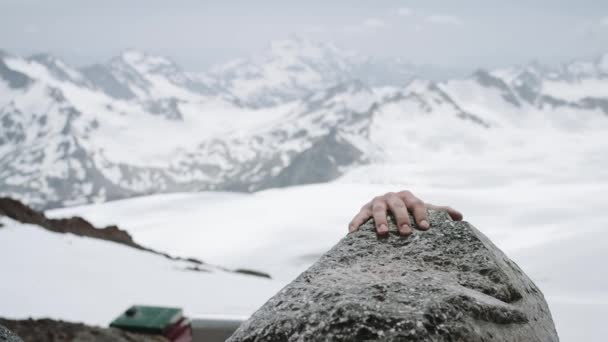 Молодой парень карабкается на скалу в снежный горный пейзаж в солнечный день — стоковое видео