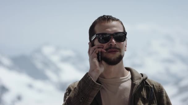 Молодой бородач на вершине горы с живописным видом разговаривает по телефону — стоковое видео