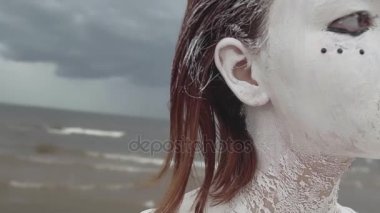 Kamera deniz kıyısında beyaz boya kaplı sanatsal kız portresi dönüşüyor