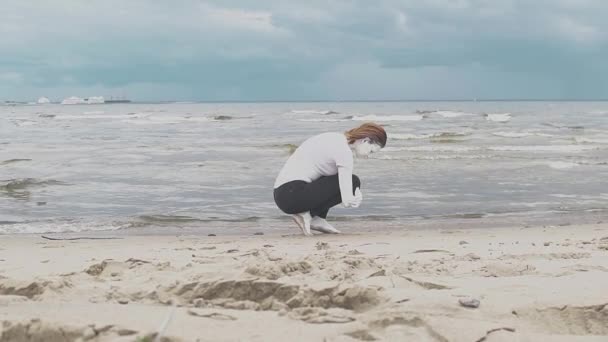 Художественная женщина, покрытая белой краской, присела на песчаном берегу моря — стоковое видео