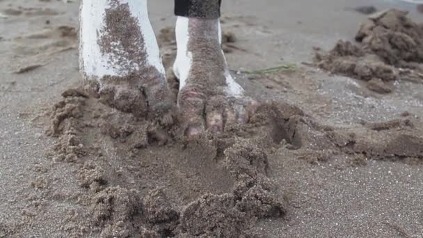 Tæer af kunstnerisk kvinde dækket af hvid maling trækker vådt sand på kysten – Stock-video