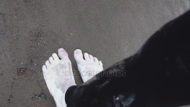 Feet of artistic person covered in white paint stand in running waves on shore — Stock Video