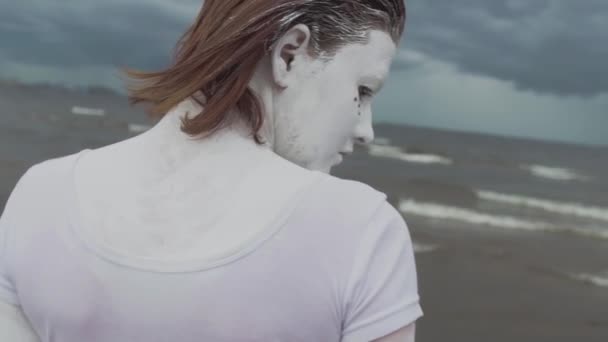 Художественная девушка, покрытая белой краской, поднимает голову на берегу моря. — стоковое видео