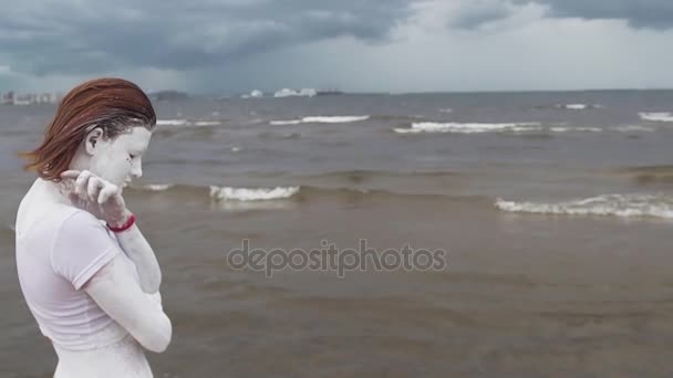 Prestanda konstnärlig kvinna täckt av vit färg kram själv vid havets strand — Stockvideo