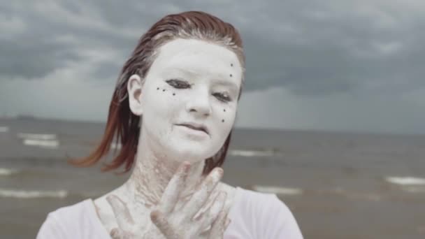 Retrato de chica artística cubierta de sonrisas de pintura blanca y bailes en la orilla del mar — Vídeo de stock