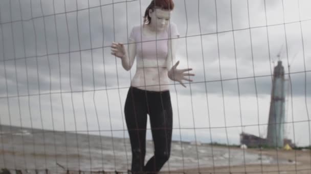 Артистка в белой краске, идущая по берегу моря вдоль металлического забора — стоковое видео