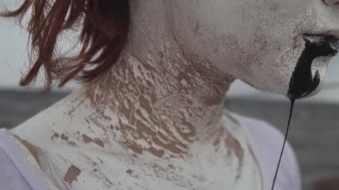 Beyaz boya kaplı aktivist sanatçı kadın deniz kıyısında siyah salya akar