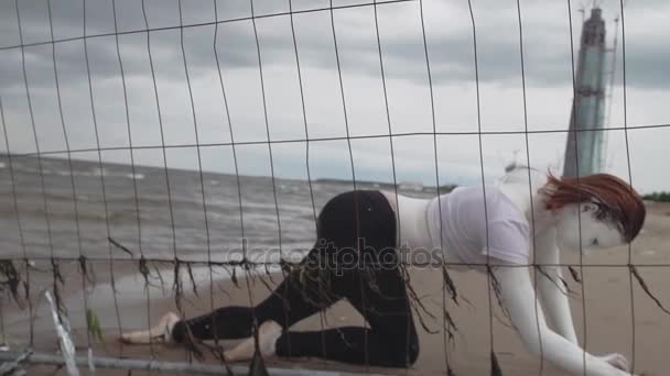 Performance artist girl in white paint crawling on sea shore along metal fence — Stock Video