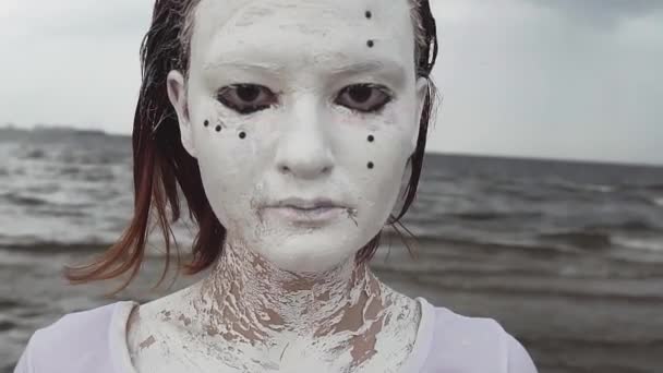 Porträt eines künstlerischen Mädchens mit weißer Farbe bedeckt, das sich am Ufer des Meeres erstreckt — Stockvideo