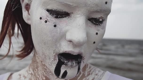 Suorituskyky taiteilija nainen peitetty valkoinen maali kuolaa musta sylkeä meren rannalla — kuvapankkivideo