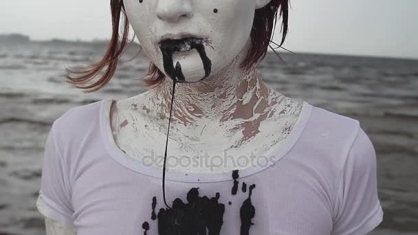 白い塗料で覆われているパフォーマンス アーティスト女性 drools 海岸に黒唾を吐く — ストック動画