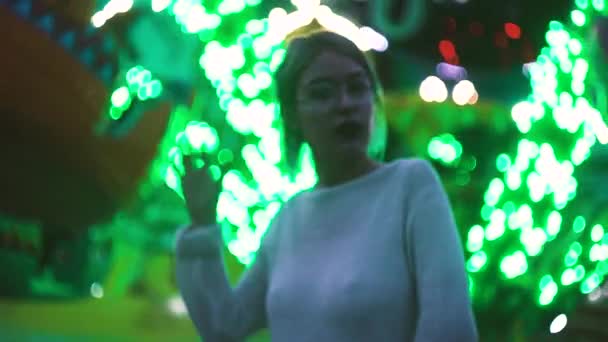 Sexig ung flicka i glasögon poserar i amusment park nära attraktion — Stockvideo