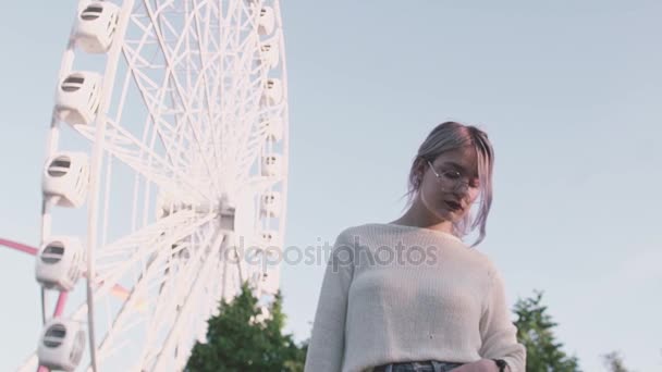 Muchacha atractiva en gafas de pie debajo de la rueda del hurón en el parque de atracciones — Vídeo de stock