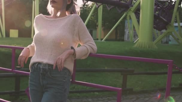 Sexig ung flicka i glasögon står nära berg-och dalbana i ljusa solen ljus — Stockvideo