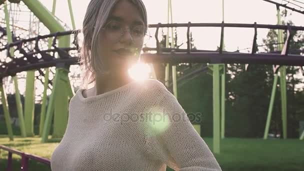 Attractive girl in glasses standing near roller coaster in bright sun flare — Stock Video