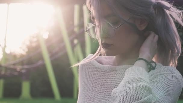 Mooi jong meisje in glazen poseren in de buurt van de achtbaan in de felle zon ray — Stockvideo