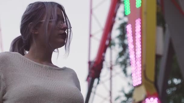 Aantrekkelijke jonge meisje in glazen staande in de buurt van swing attractie in amusment park — Stockvideo