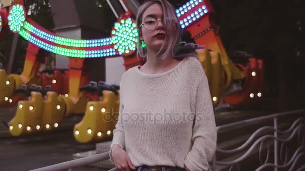 Menina bonita em óculos posando perto de atração swing no parque de diversões — Vídeo de Stock