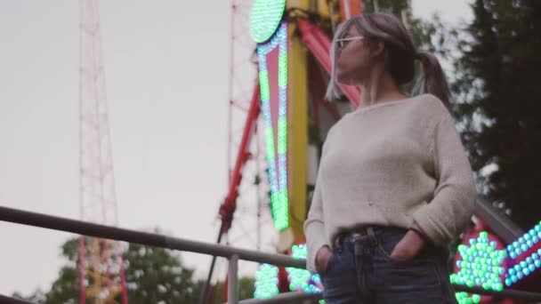 Jovem atraente em óculos posando perto de atração swing no parque de diversões — Vídeo de Stock