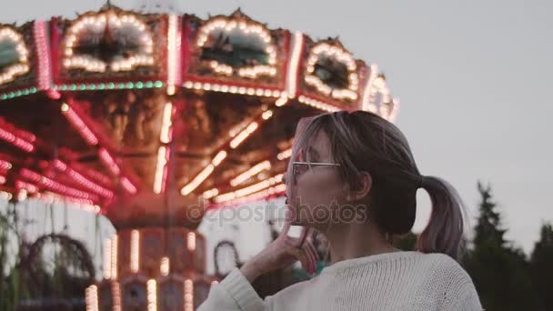 Привлекательная девушка в очках позирует возле аттракциона карусели в парке аттракционов — стоковое видео