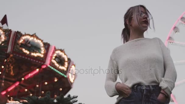 Hipster ung flicka i glasögon står nära carousel attraktion i amusment park — Stockvideo