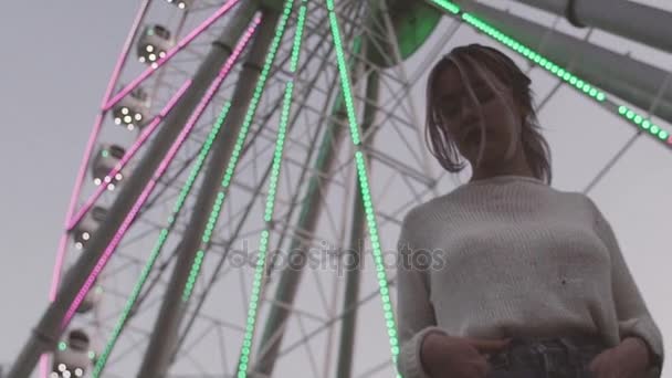 Menina bonita em óculos de pé sob a roda de observação com luzes piscando — Vídeo de Stock