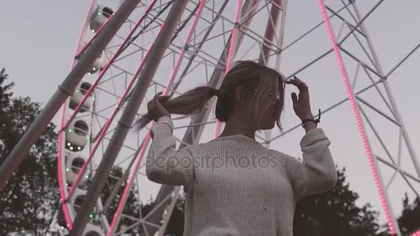Aantrekkelijk meisje in glazen permanent onder reuzenrad met knipperende lichten — Stockvideo