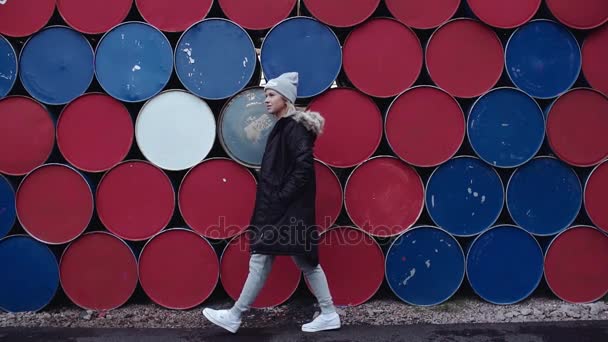 Chica rubia joven camina delante de la pila de barriles de colores — Vídeo de stock